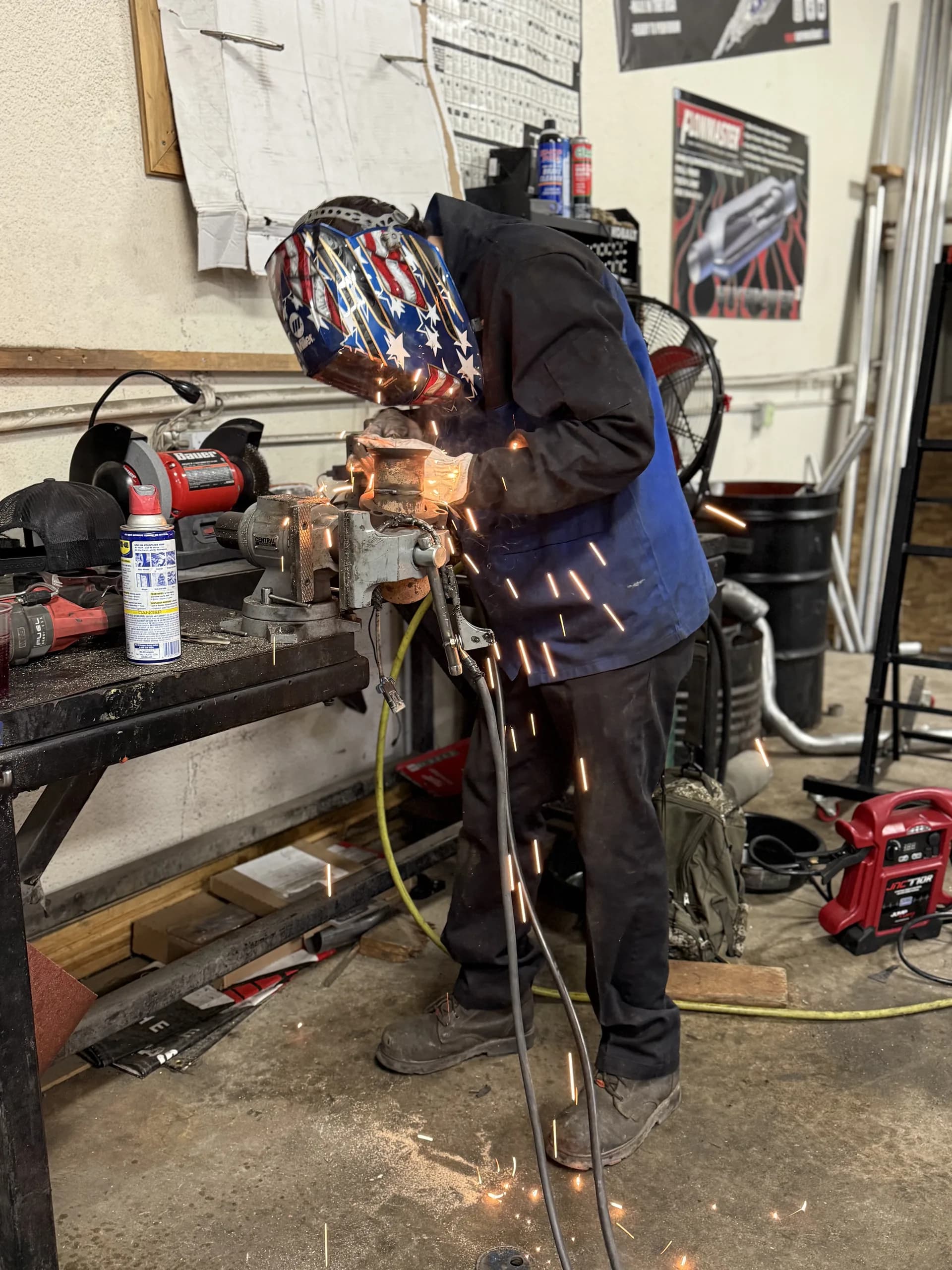 muffler shop welding exhaust component with patriotic helmet