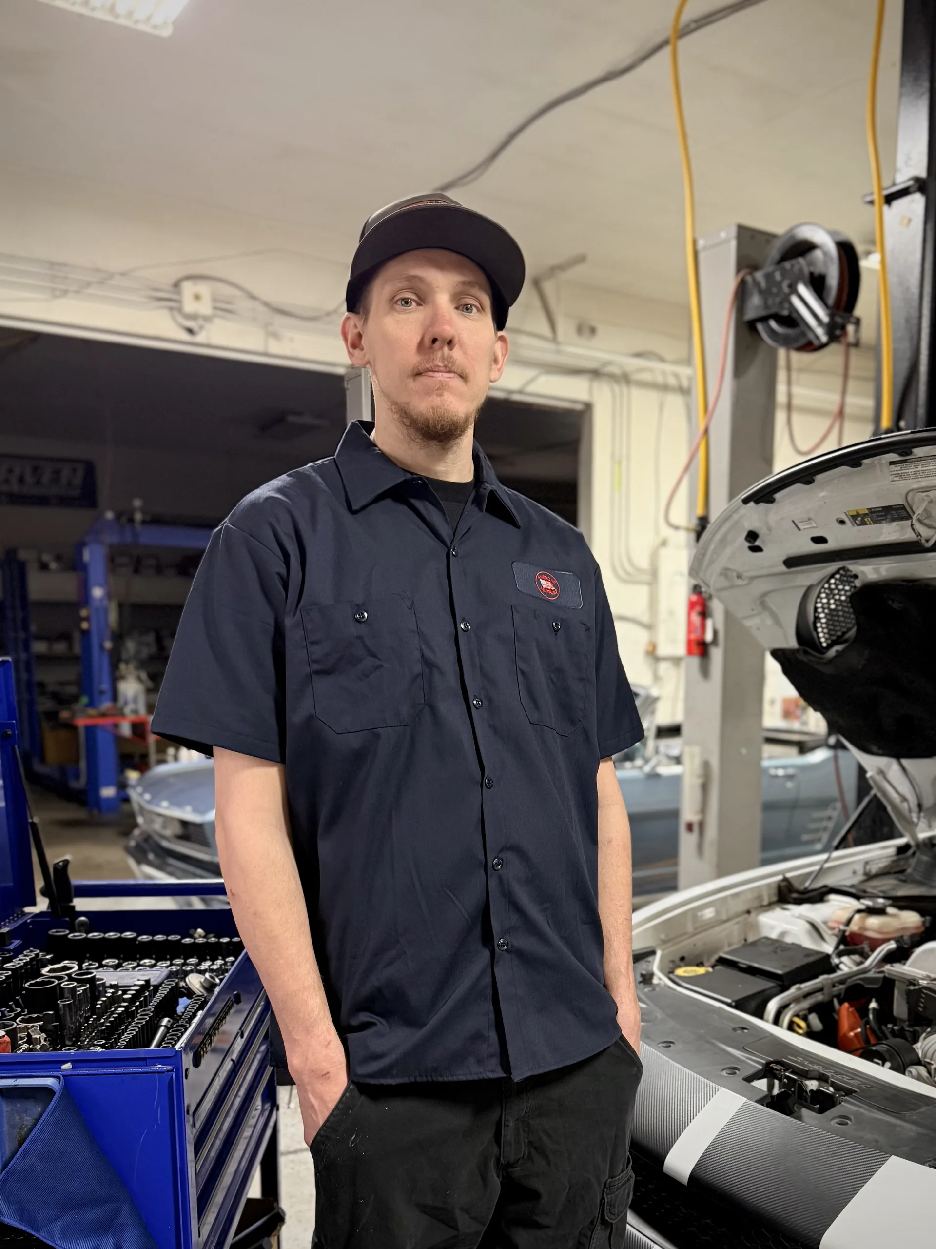 owner mechanic standing in auto repair shop with hood open